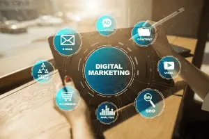 Hands holding a tablet with a teal "Digital Marketing" hub ringed by E-mail, Social Media, SEO, E-commerce and Ad icons.