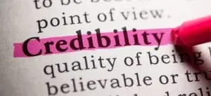 Close-up of a dictionary page with the word "Credibility" highlighted in pink marker above its definition, "quality of being believable"