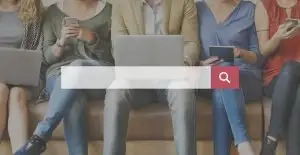 Five people seated on a bench using phones, a laptop and a tablet, with a large white search bar and red magnifying glass button across them