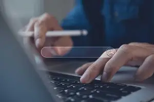Close-up of hands at a laptop keyboard holding a stylus, with a thin white search bar and magnifying glass icon overlaid