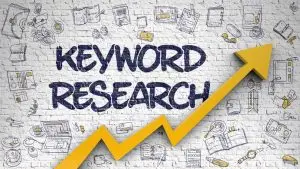 "KEYWORD RESEARCH" painted on a white brick wall beside a rising yellow arrow, framed by hand-drawn doodles of laptops, books and coffee cups.