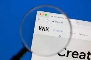 Magnifying glass held over a screen showing the wix.com homepage, with the Wix logo and the Creation and Growth menu links visible.