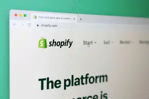 Close-up photo of a computer screen angled to show the shopify.com homepage, its green shopping-bag logo and the headline "The platform"
