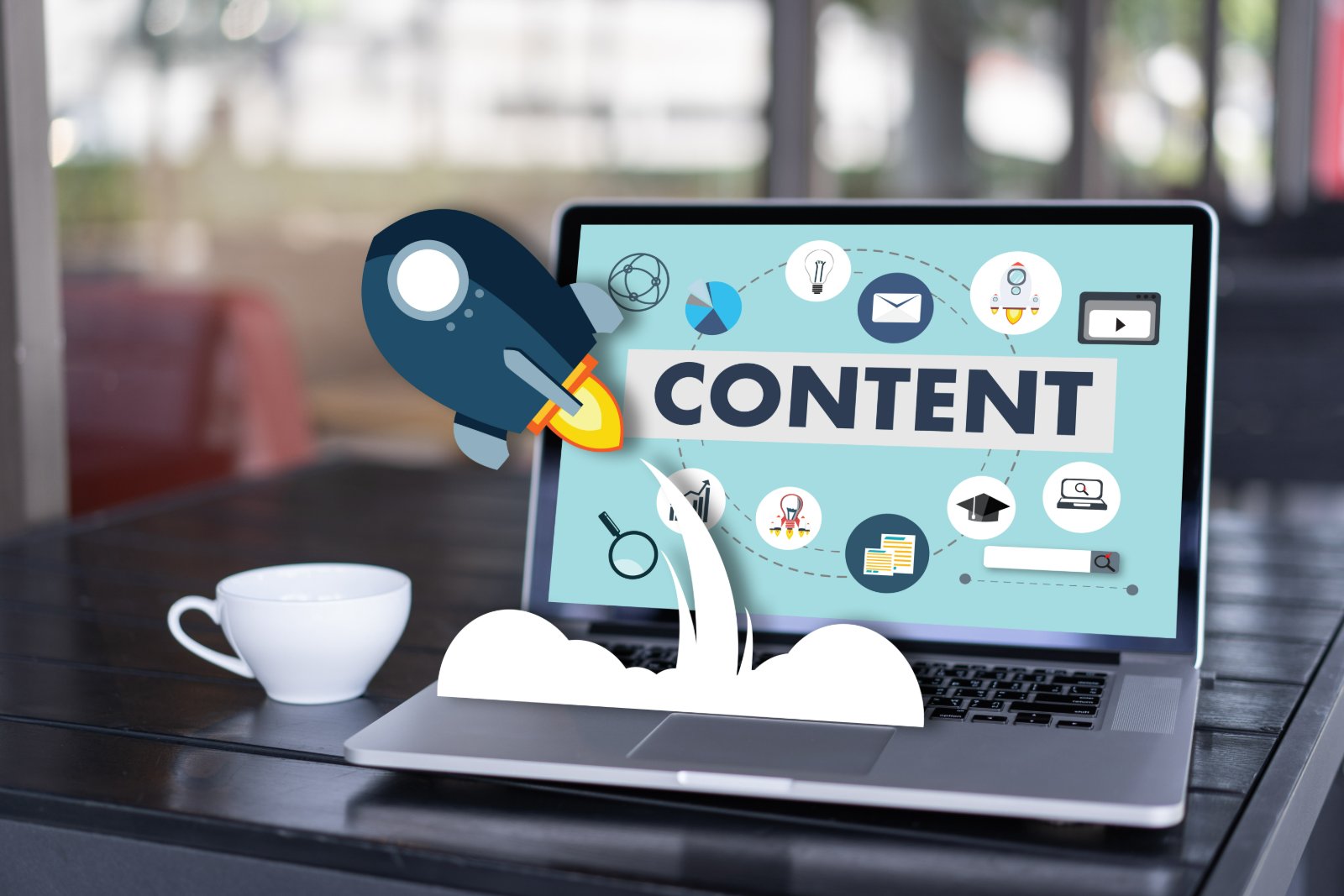 Laptop on a desk with a content launch illustration — a rocket lifting off beside the word CONTENT surrounded by blog, email, video, and search icons