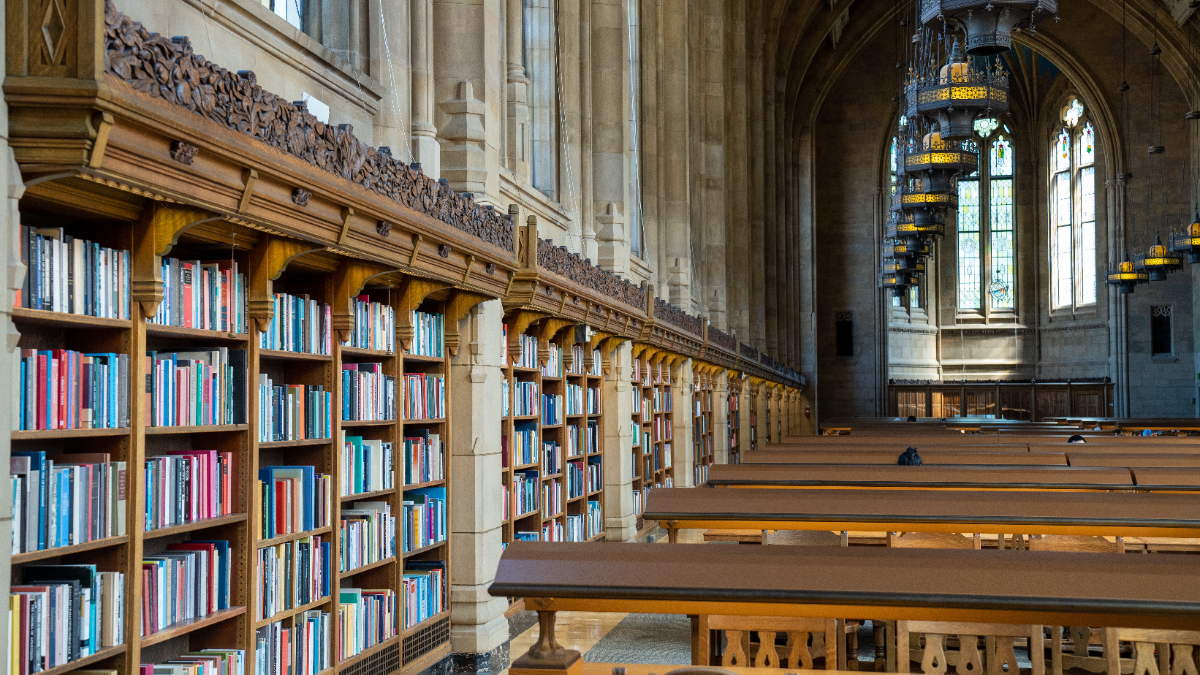 Gothic university library reading room with tall bookshelves, stained-glass windows, and long study tables
