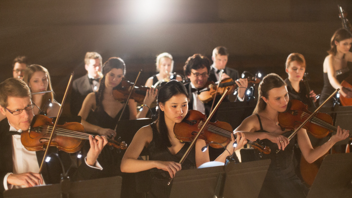 Orchestra string section performing in concert dress under stage lighting